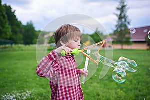 Outdoors portrait of cute preschool boy blowing soap bubbles on a green lawn at the playground