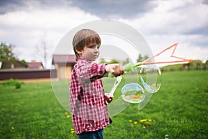 Outdoors portrait of cute preschool boy blowing soap bubbles on a green lawn at the playground