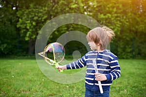 Outdoors portrait of cute preschool boy blowing soap bubbles on a green lawn at the playground