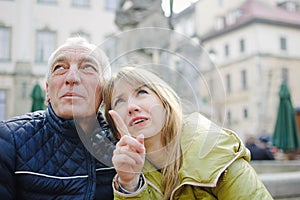 Outdoors portrait of elderly man and his young blonde wife spending time together in the ancient city during early