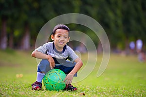 Outdoors portrait at grass city park of 5 years old Asian Indonesian child smiling happy and cheerful sitting on ball laughing