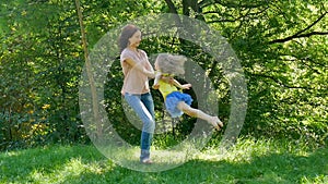 Outdoors Portrait of Happy Young Mother in Pink Shirt and Jeans Swirling her Cute Little Daughter in the Park during