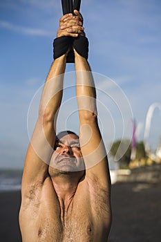 Outdoors portrait of  man practicing aero yoga workout at the beach hanging from rope swing above the sea training body balance