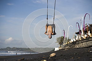 Outdoors portrait of  man practicing aero yoga workout at the beach hanging from rope swing above the sea training body balance