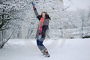 Outdoors portrait of smiling young girl wearing red scarf and having fun outside in the snowy park during winter time.