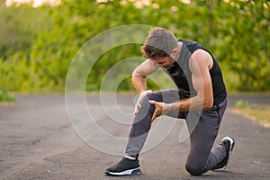 Outdoors portrait of young attractive sport man in pain touching his knee suffering ligaments accident or some injury during