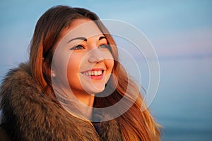 Outdoors portrait of young beautiful smiling girl with red cheeks in winter near the frozen lake