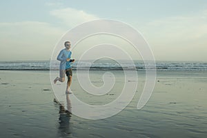 Outdoors running workout - young attractive and athletic runner man jogging on beautiful beach in Summer training happy and free