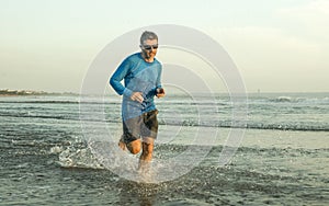 Outdoors running workout - young attractive and athletic runner man jogging on beautiful beach in Summer training happy and free