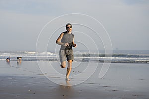 Outdoors running workout - young attractive and athletic runner man jogging on beautiful beach in Summer training happy and free