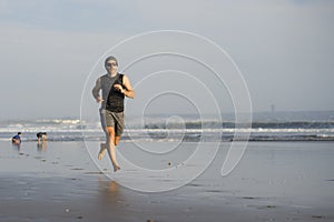 Outdoors running workout - young attractive and athletic runner man jogging on beautiful beach in Summer training happy and free