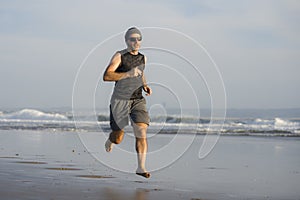 Outdoors running workout - young attractive and athletic runner man jogging on beautiful beach in Summer training happy and free