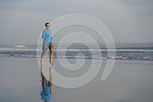 Outdoors running workout - young attractive and athletic runner man jogging on beautiful beach in Summer training happy and free