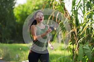 Outdoors running workout - young happy and dedicated Asian Chinese woman jogging at beautiful city park or countryside trail on