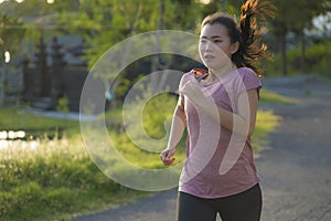 Outdoors running workout - young happy and dedicated Asian Japanese woman jogging at beautiful city park or countryside trail on