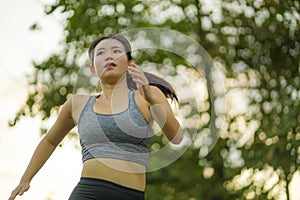 Outdoors running workout - young happy and dedicated Asian Korean woman jogging at beautiful city park or countryside trail on