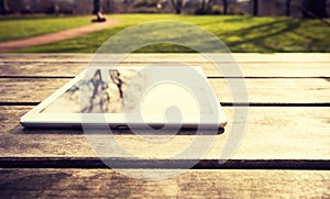 Outdoors rustic wooden table with digital tablet, reflecting trees, with copy space