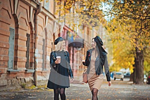 Outdoors shot of young women with coffee on city street. Two fashion girls walking outdoor with cofee. Streetfashion friends