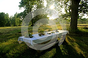 Outdoors summer scene party table on sunset. Old wooden table under trees with food plate. Midsummer celebrating in Latvia