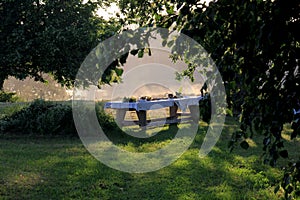 Outdoors summer scene party table on sunset. Old wooden table under trees with food plate. Midsummer celebrating in Latvia