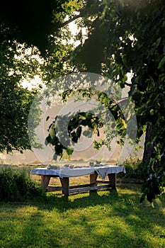 Outdoors summer scene party table on sunset. Old wooden table under trees with food plate. Midsummer celebrating in Latvia