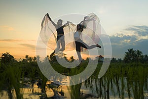Outdoors sunset acroyoga workout - couple of young happy and fit women practicing acro yoga drill with wings at beautiful rice