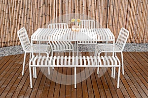 Outdoors white steel table and chairs on a wooden terrace