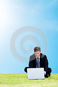 Outdoors working - Businessman on green grass with a laptop. Happy young businessma sitting on grass and working on