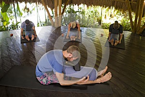 Outdoors yoga lesson - group of young people and coach man practicing relaxation exercise at Asian wellness retreat hut training