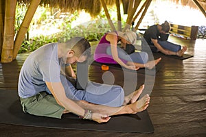 Outdoors yoga lesson - group of young people and coach woman practicing relaxation exercise at Asian wellness retreat hut training