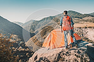 Outdoorsman traveler with backpack stands on cliff with his tent with a gorgeous view of a mountain valley in Armenia. Camping