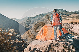 Outdoorsman traveler with backpack stands on cliff with his tent with a gorgeous view of a mountain valley in Armenia. Camping photo