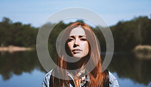 Outdoorsy young woman standing by lake in harsh light