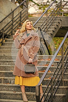 Outerwear of modern warm and stylish eco fur. Girl warm coat stand urban stairs background. Create fall outfit to feel