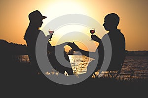 Outline of young couples relaxing on the bank of the river at dawn with a glass of wine on the chairs