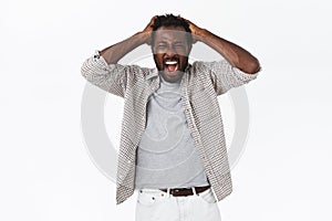 Outraged and distressed african-american bearded man yelling from grief and loss, holding hands on head, shouting with