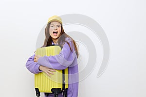 outraged, the woman stands on a white background in a purple tracksuit and a yellow cap, she gripped the suitcase with
