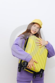 outraged, the woman stands on a white background in a purple tracksuit and a yellow cap, she gripped the suitcase with