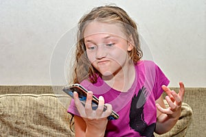 An outraged and worried girl angrily looks at the phone, waving her arms