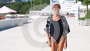 Outside closeup portrait Beautiful stylish sporty woman in black swimsuit and white cap walking along bay seaside