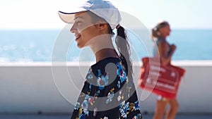 Outside closeup portrait Beautiful stylish sporty woman in black swimsuit and white cap walking along bay seaside