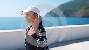 Outside closeup portrait Beautiful stylish sporty woman in black swimsuit and white cap walking along bay seaside