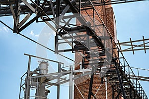 An outside industrial conveyer belt at an old tobacco factory with bright blue sky and a brick smoke tower.