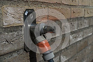 Outside metal water tap sticking out of normal house wall bricks. House water tap with a waterhose attached. Macro close up shot