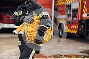 Outside near truck and with fire hose in hands. Woman in uniform is at work in department