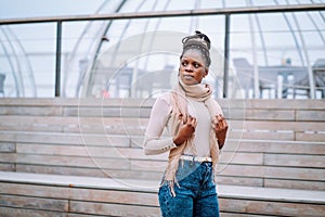 Outside portrait of Afro-American woman in beige scarf and roll-neck sweater with long afro braids gathered in bun.