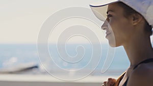 Outside portrait of Beautiful stylish sexy sporty woman in black swimsuit and white cap walking along bay at seaside