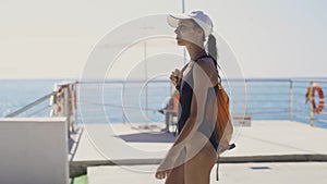 Outside portrait of Beautiful stylish sexy sporty woman in black swimsuit and white cap walking along bay at seaside