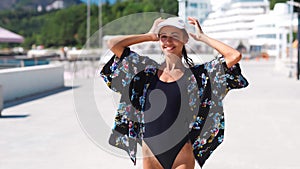 Outside portrait Beautiful stylish sporty woman in black swimsuit and white cap walking along bay seaside