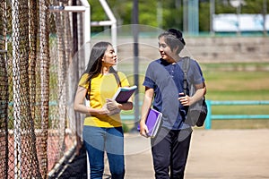 Outside of school, a happy young couple of students stands along a fence, studying a book